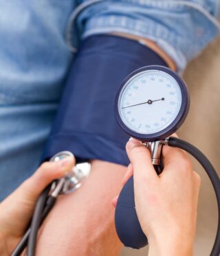 Close-up of a blood pressure check, showing a cuff wrapped around a person's arm and a manual blood pressure gauge being used to take a reading.
